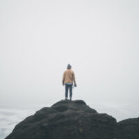 A man stands on a rocky mountain under a white sky